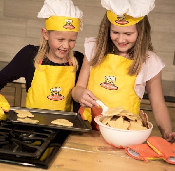 One girl holding a pan of cookies while the other transfers them to a bowl with a spatula.