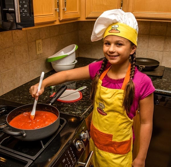 A girl stirring spaghetti sauce over the stove.
