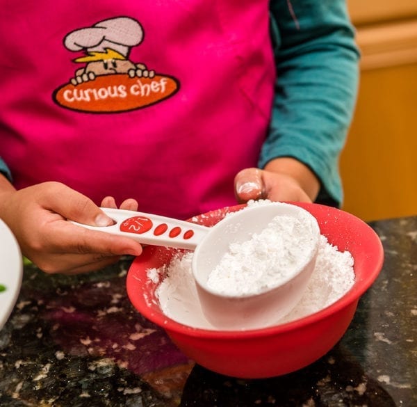 A measuring cup of flour from a red bowl filled with flour.