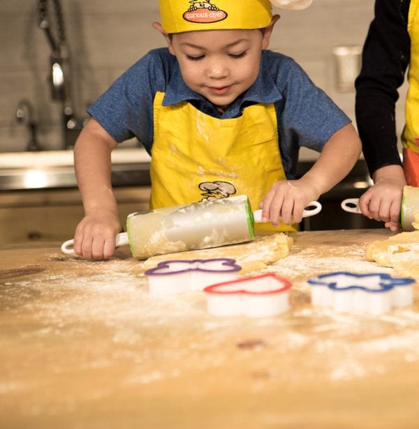 A boy rolling out dough with a rolling pin.